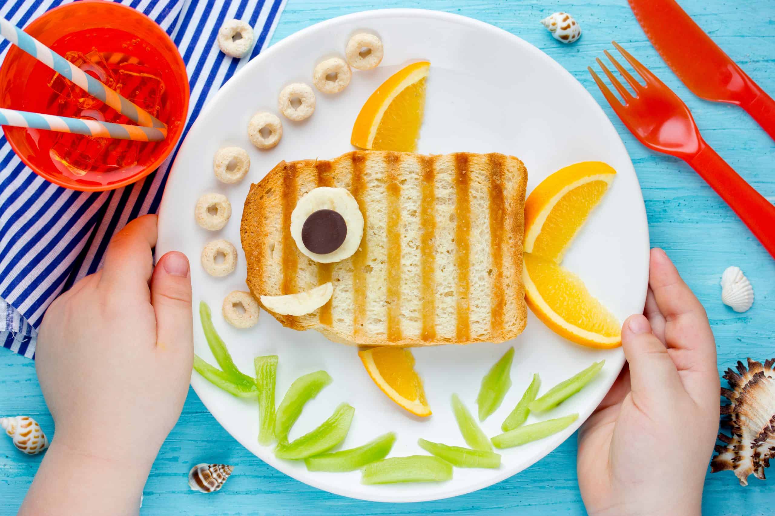 Child's hands hold plate with Funny Fish Sandwich Craft on it (food made to look like a cute fish)