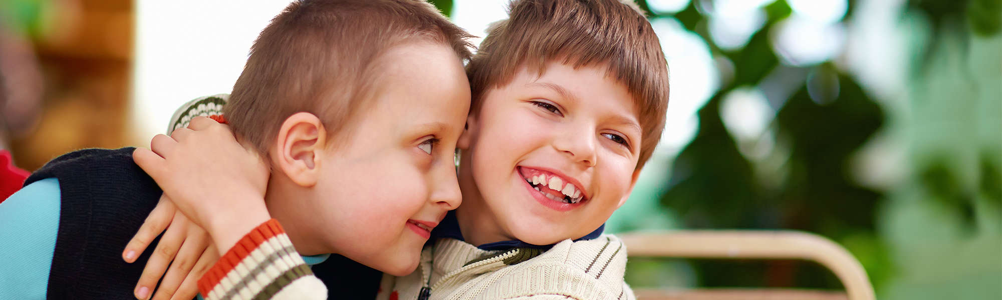 Two young boys with disabilities hug and smile widely