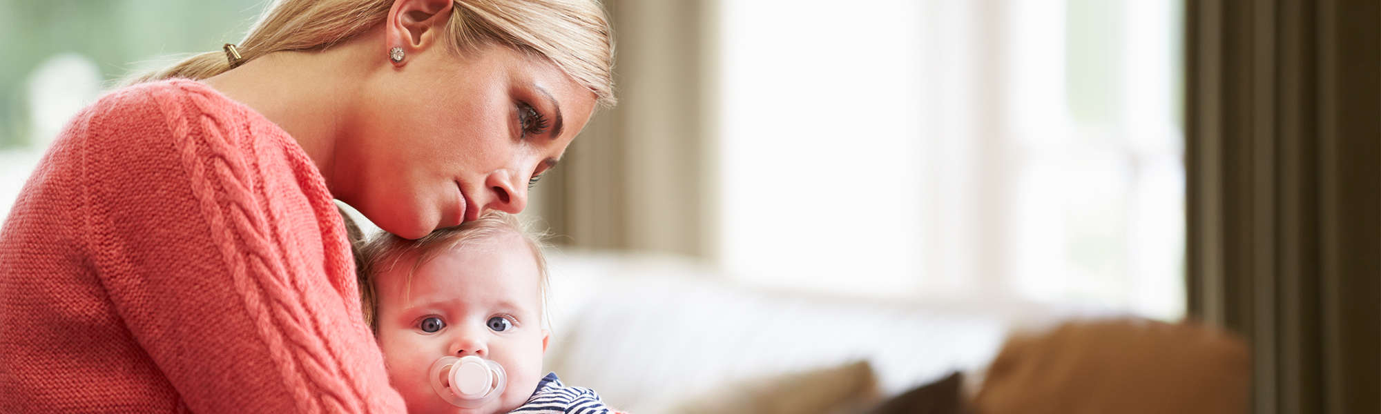 Blonde woman holds baby daughter with vague worried look on her face