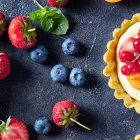 Birds eye view of sweet summer tarts covered in berries, next to big bowl of berries and fruit