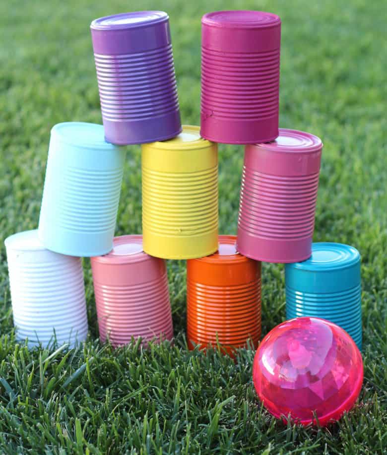 Painted tin cans stacked on eachother on grass outside, next to small pink ball