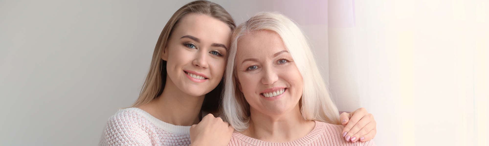 Younger daughter and older lady partially hug and smile at camera