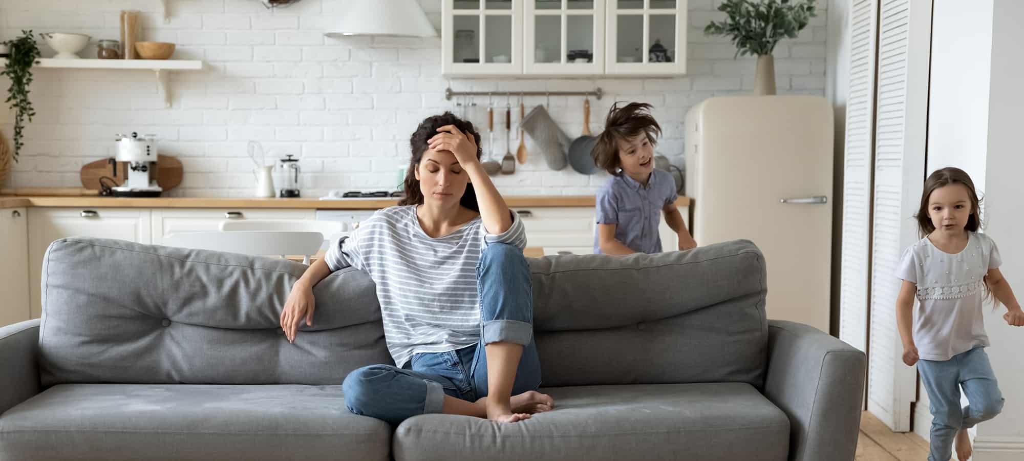 woman with low tolerance levels sits on couch frustrated as children run around her